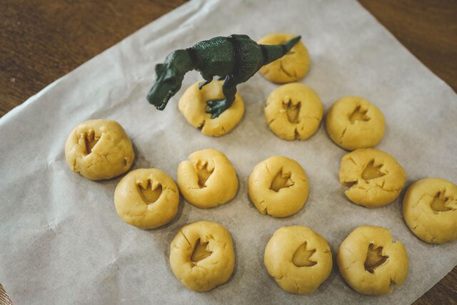 Dinosaur toy making footprints in cookie dough on a baking tray during a fun Dino Discovery Day activity.